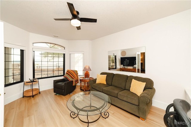 living area with baseboards, ceiling fan, visible vents, and light wood finished floors