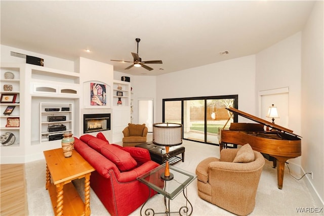 living area featuring ceiling fan, built in shelves, visible vents, baseboards, and a glass covered fireplace