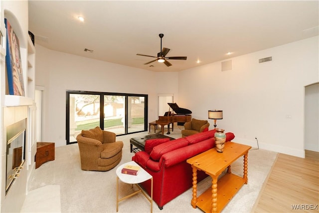 living area featuring baseboards, visible vents, a ceiling fan, light wood-style floors, and a fireplace