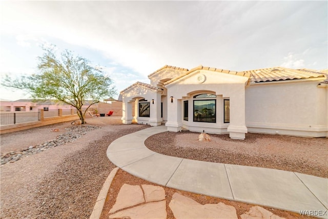 mediterranean / spanish home featuring a tile roof, fence, and stucco siding