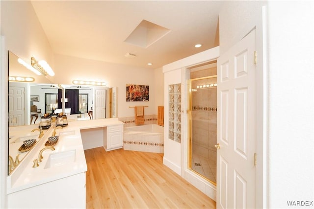 bathroom featuring wood finished floors, a sink, a bath, double vanity, and a stall shower