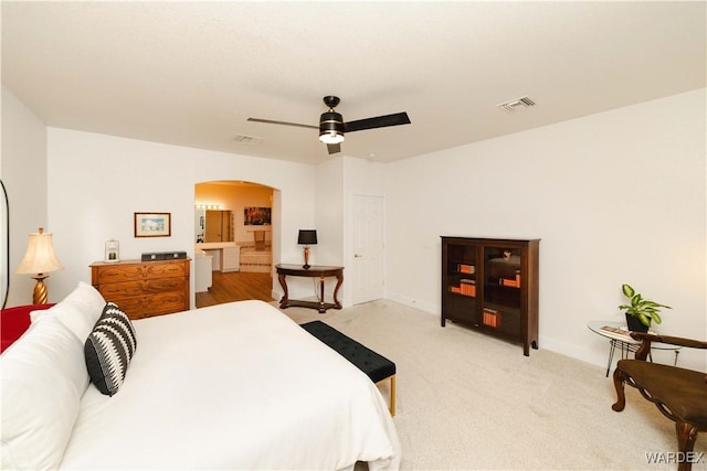 bedroom with light carpet, ceiling fan, visible vents, and arched walkways