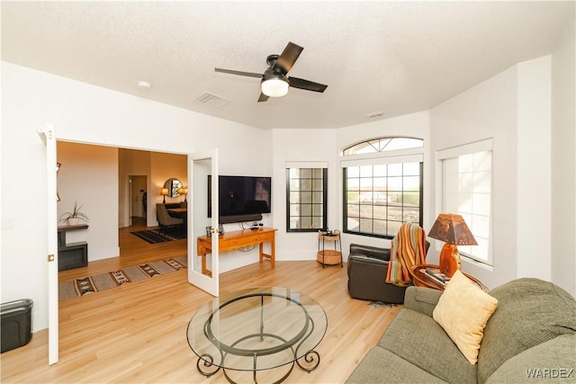 living room with ceiling fan, a textured ceiling, wood finished floors, and visible vents