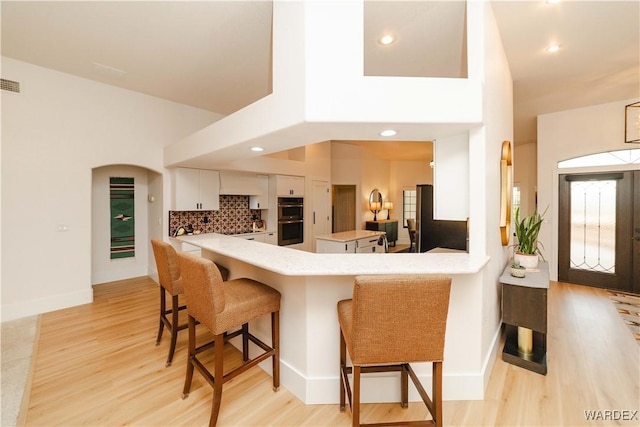 kitchen with double wall oven, white cabinetry, a peninsula, and a kitchen breakfast bar