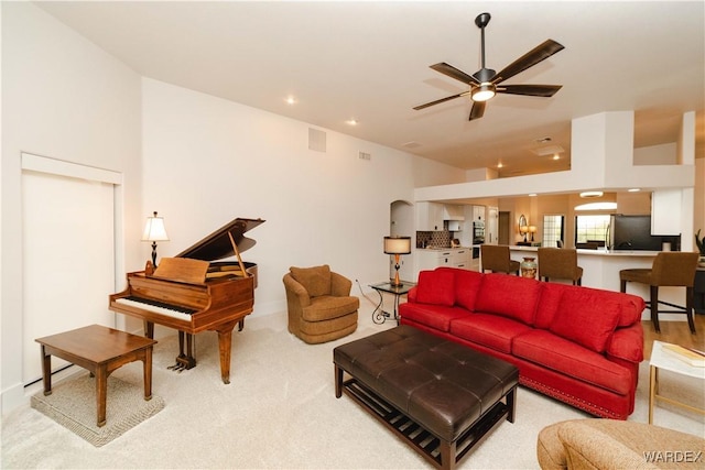 living area featuring ceiling fan, visible vents, arched walkways, and light colored carpet