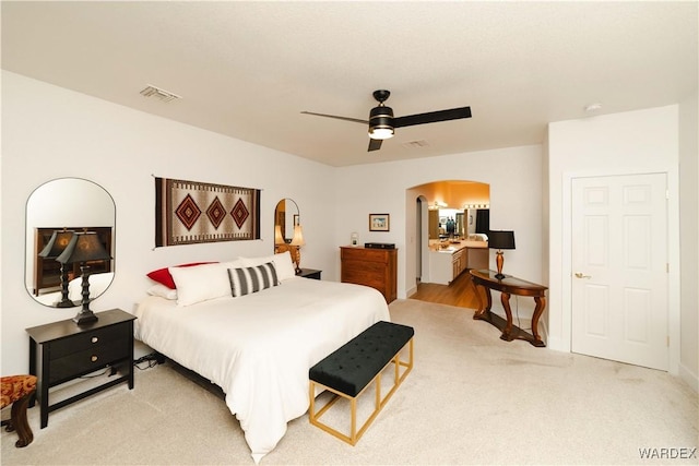 bedroom featuring light colored carpet, arched walkways, visible vents, and ceiling fan