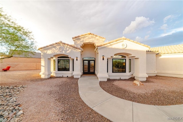 mediterranean / spanish-style home with french doors, a tile roof, and stucco siding