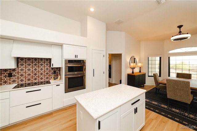 kitchen with white cabinets, a kitchen island, stainless steel double oven, stovetop, and light wood-type flooring