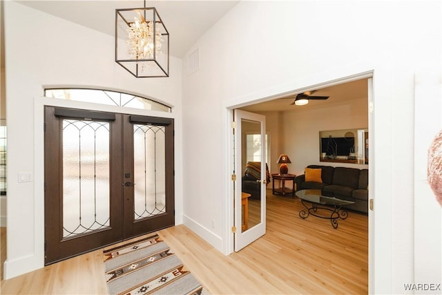 entrance foyer with a notable chandelier, a high ceiling, wood finished floors, baseboards, and french doors