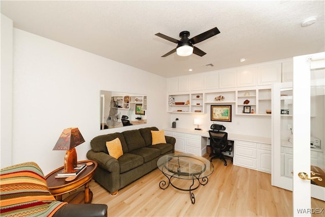 living area featuring light wood-style flooring, visible vents, ceiling fan, and built in desk