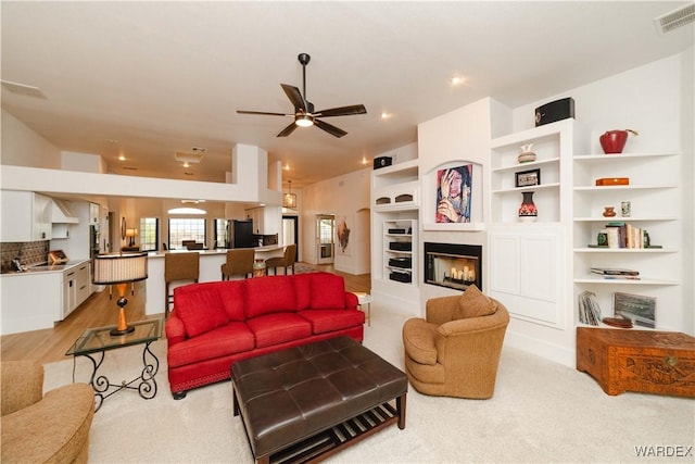 living area with vaulted ceiling, a glass covered fireplace, visible vents, and a ceiling fan