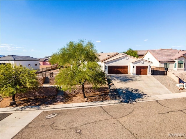 view of front of house with stucco siding, concrete driveway, an attached garage, fence, and a residential view