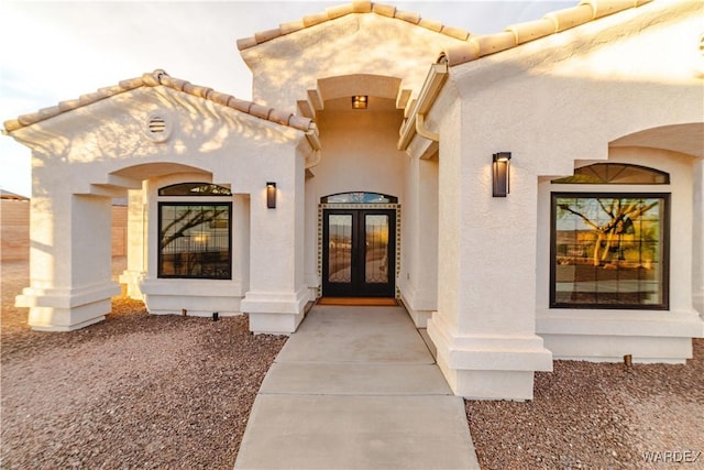 entrance to property with a tiled roof, french doors, and stucco siding