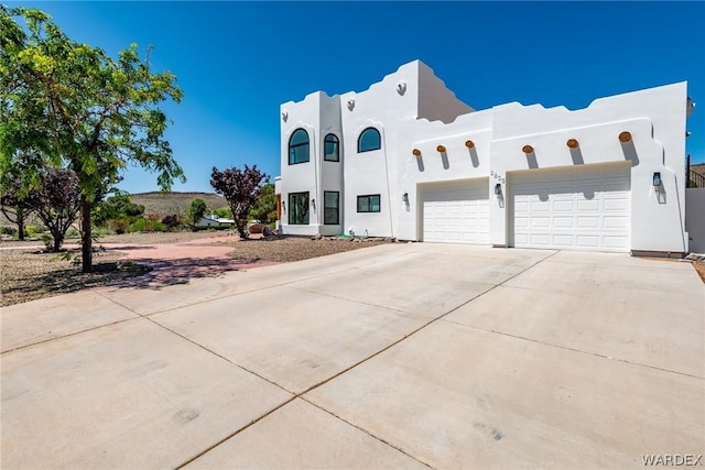 pueblo revival-style home with a garage, concrete driveway, and stucco siding