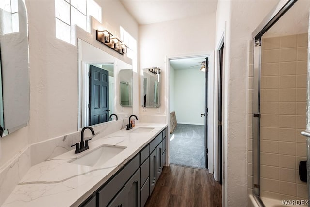 full bathroom featuring ceiling fan, double vanity, a sink, and wood finished floors