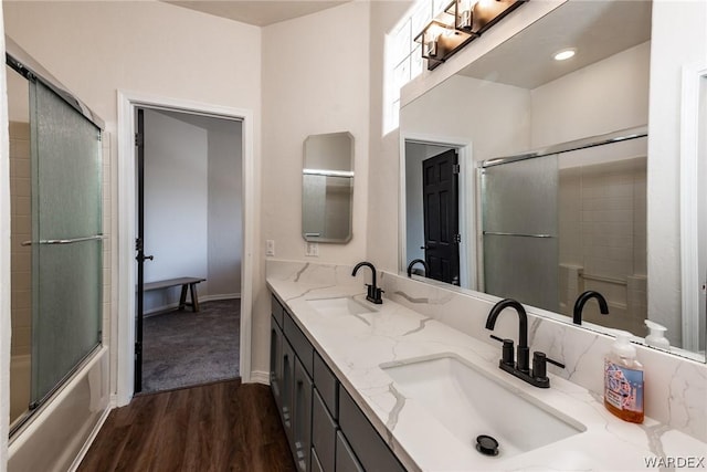 full bathroom with double vanity, bath / shower combo with glass door, a sink, and wood finished floors