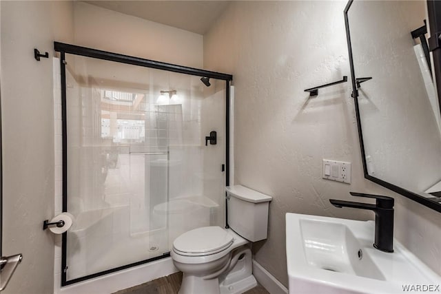 full bath with a textured wall, a stall shower, a sink, and toilet