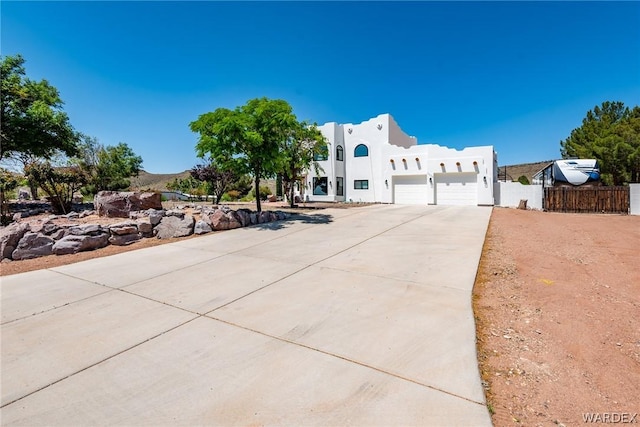 pueblo-style home with a garage, fence, driveway, and stucco siding