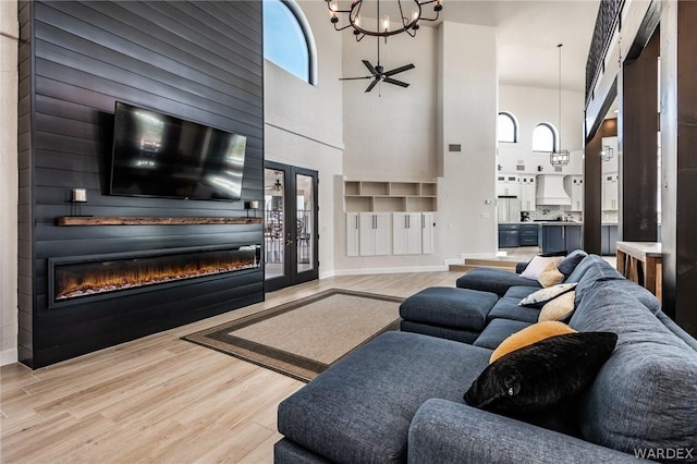 living room featuring baseboards, a glass covered fireplace, light wood-type flooring, built in shelves, and a chandelier