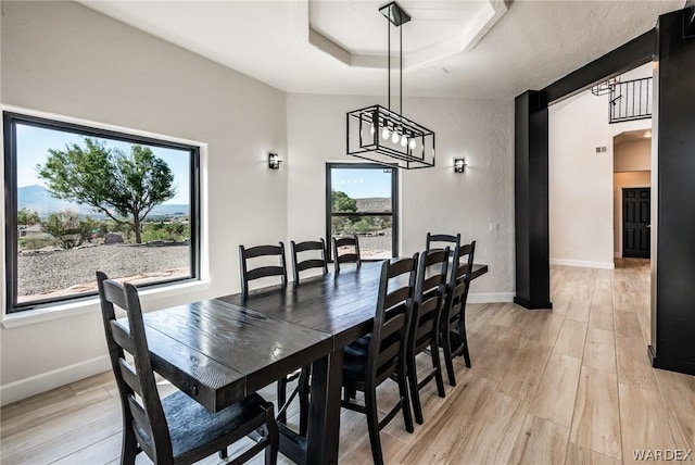 dining space with light wood finished floors, baseboards, and a tray ceiling