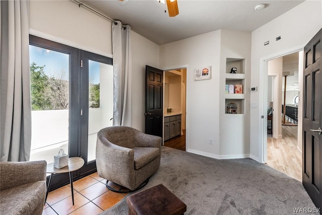 sitting room featuring built in features, light carpet, baseboards, and a ceiling fan