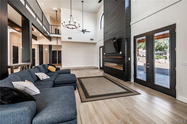 living room featuring baseboards, a towering ceiling, french doors, light wood-type flooring, and a chandelier