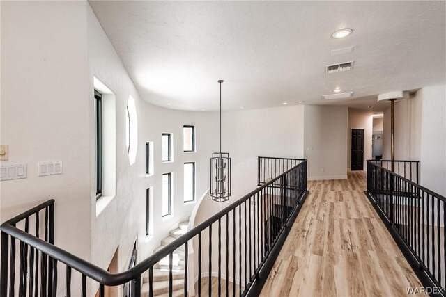 hall featuring visible vents, light wood-style flooring, an upstairs landing, and baseboards