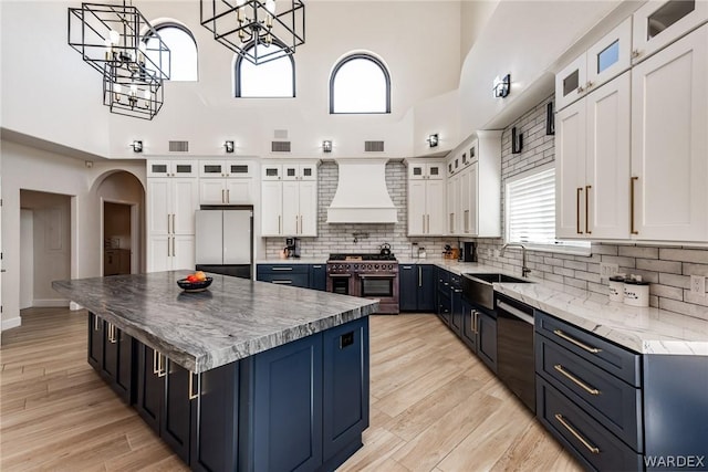 kitchen featuring custom range hood, glass insert cabinets, freestanding refrigerator, white cabinets, and double oven range