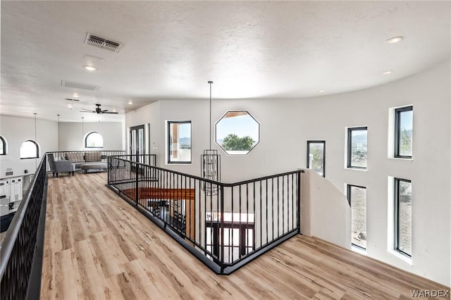 corridor featuring light wood finished floors, visible vents, a textured ceiling, and an upstairs landing