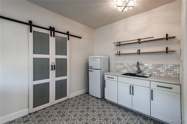 kitchen featuring open shelves, light countertops, a barn door, white cabinetry, and a sink