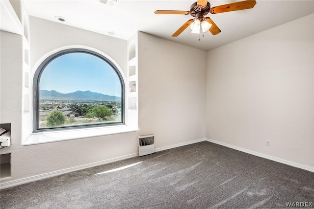 carpeted spare room featuring heating unit, baseboards, a mountain view, and a ceiling fan