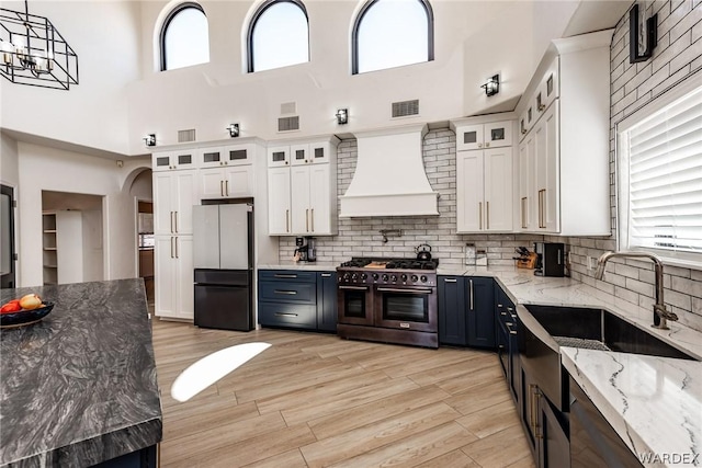 kitchen featuring pendant lighting, white cabinets, freestanding refrigerator, double oven range, and custom range hood