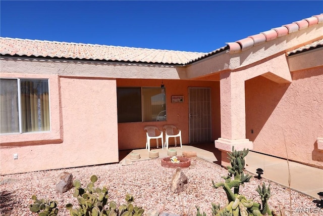 view of exterior entry featuring a patio area, a tile roof, and stucco siding