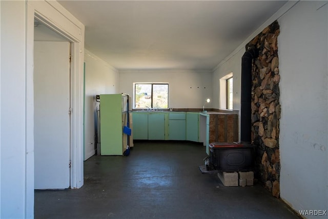 kitchen with a wood stove, green cabinets, crown molding, and freestanding refrigerator