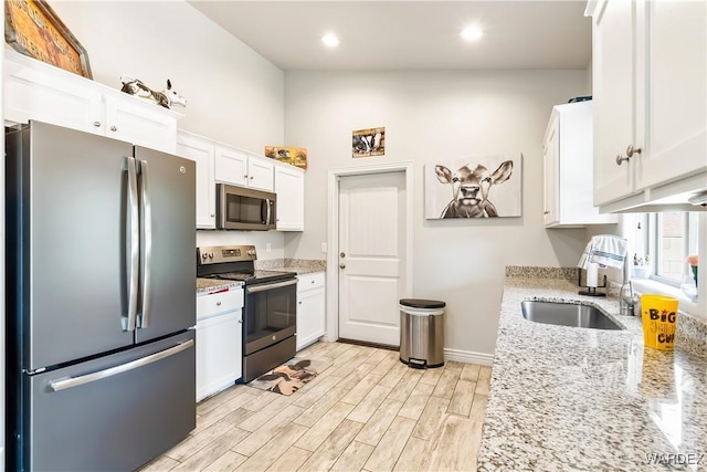 kitchen featuring light stone counters, a sink, white cabinets, appliances with stainless steel finishes, and light wood-type flooring