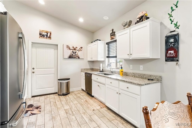 kitchen with white cabinets, light stone counters, stainless steel appliances, light wood-type flooring, and a sink