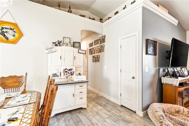 kitchen with arched walkways, white cabinets, lofted ceiling, dark countertops, and light wood-style flooring