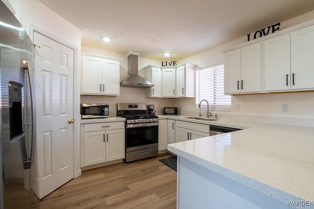 kitchen featuring white cabinets, stainless steel appliances, light wood-style flooring, a sink, and wall chimney range hood