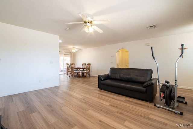living area featuring a ceiling fan, light wood-style floors, arched walkways, baseboards, and visible vents