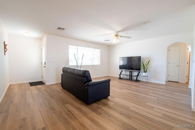 living room with visible vents, a ceiling fan, arched walkways, light wood-type flooring, and baseboards