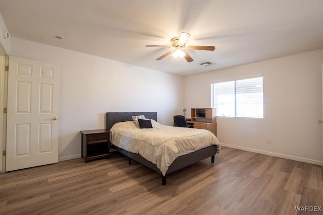 bedroom with wood finished floors, visible vents, a ceiling fan, and baseboards