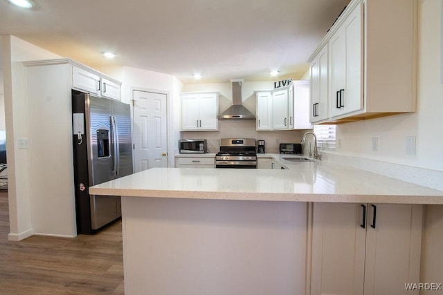 kitchen with stainless steel appliances, wall chimney range hood, a sink, a peninsula, and light wood-style flooring