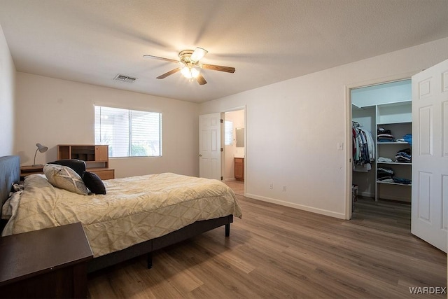 bedroom with wood finished floors, visible vents, a walk in closet, baseboards, and ceiling fan