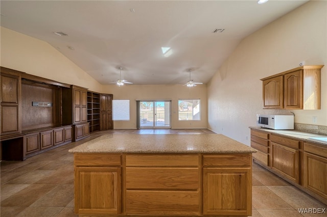 kitchen with visible vents, white microwave, a ceiling fan, a kitchen island, and vaulted ceiling