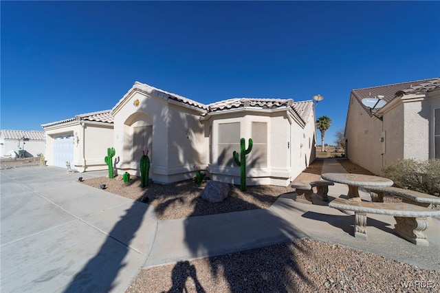 view of side of home with driveway, a tiled roof, an attached garage, and stucco siding