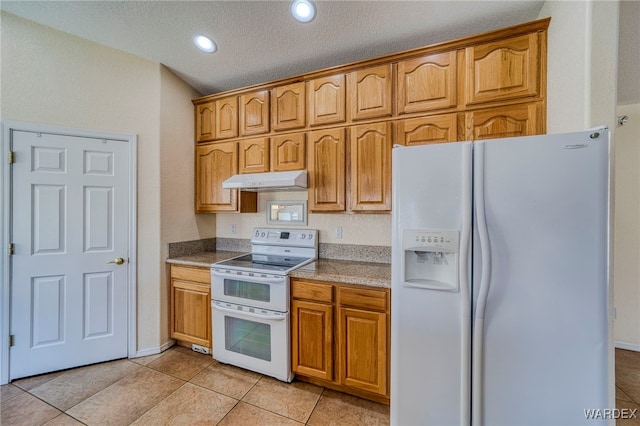 kitchen featuring a textured ceiling, light tile patterned flooring, under cabinet range hood, white appliances, and brown cabinets