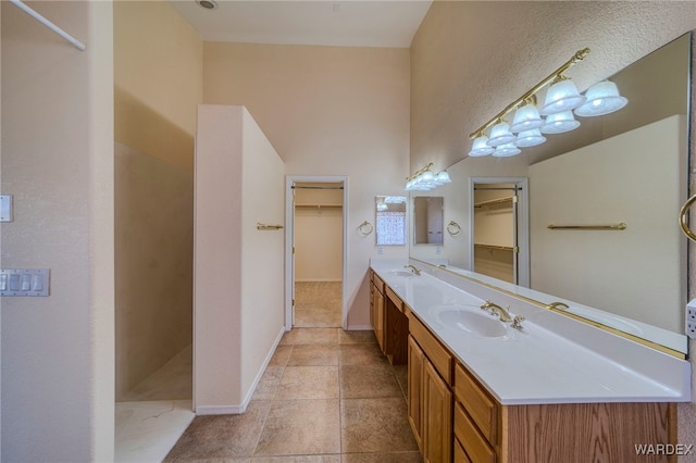 bathroom with double vanity, walk in shower, a sink, and baseboards