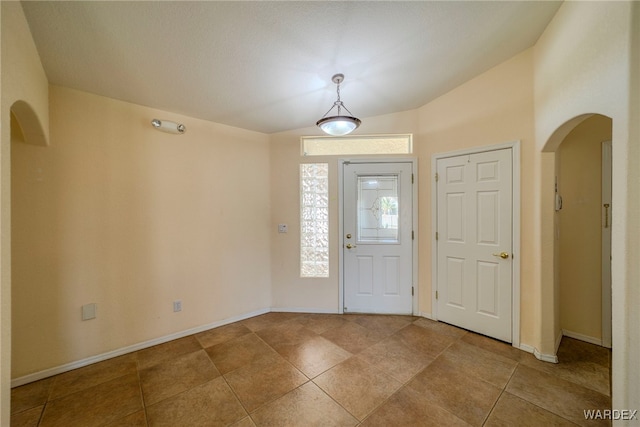 foyer featuring baseboards, arched walkways, and tile patterned floors