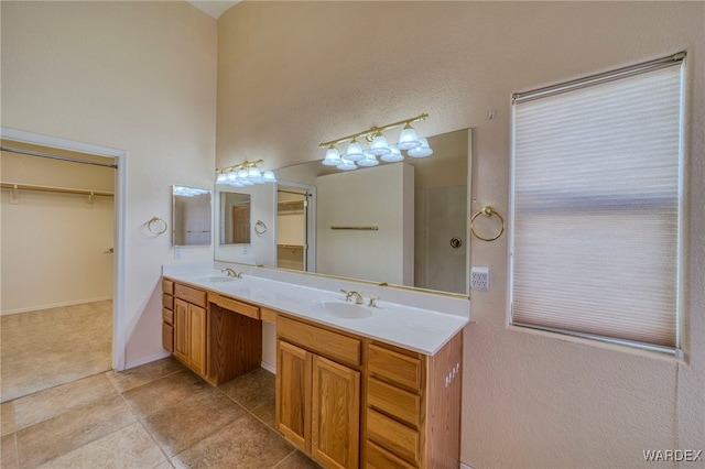 full bath with double vanity, a sink, a walk in closet, and tile patterned floors