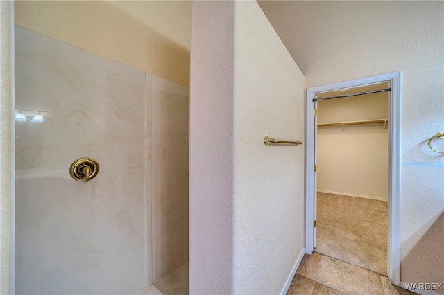 bathroom with a spacious closet, baseboards, and walk in shower